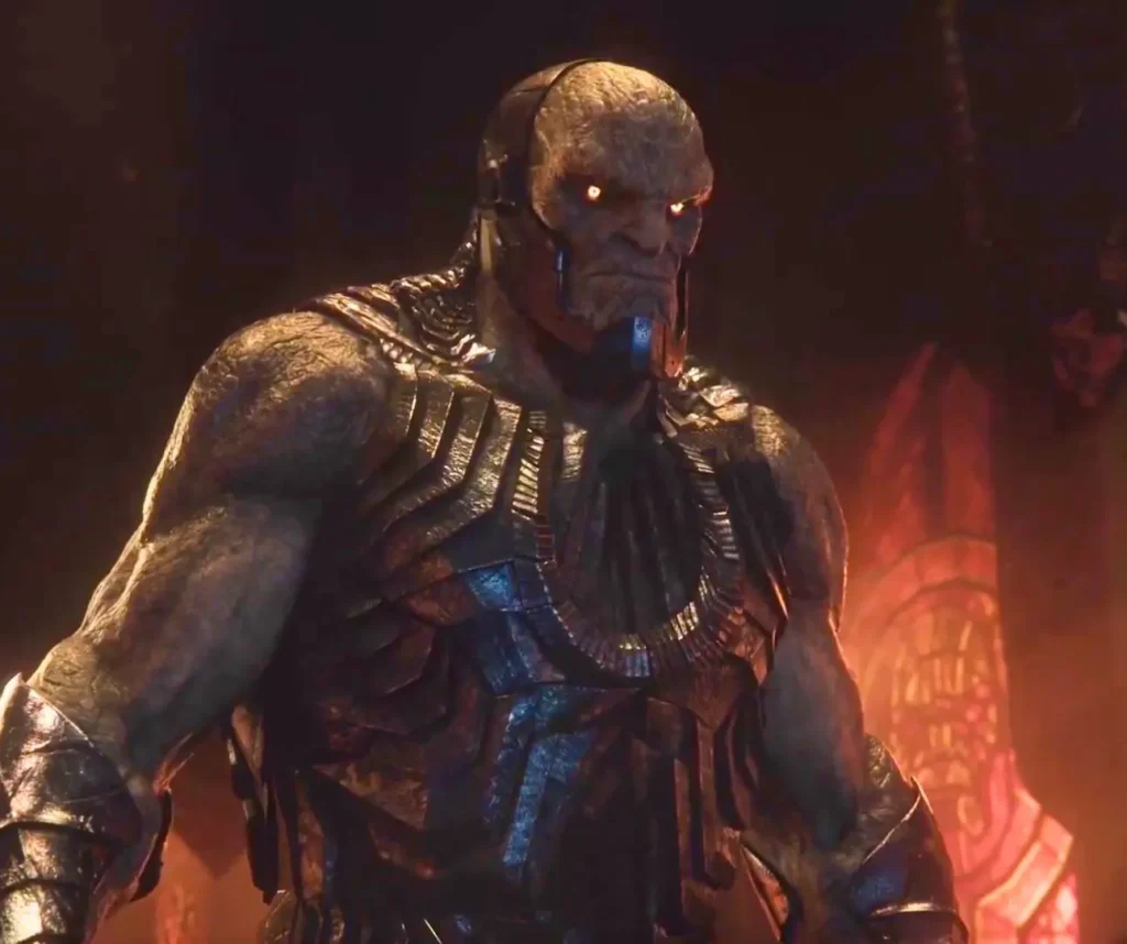 Darkseid in full New God armor with blue accents and glowing red eyes against fiery battlefield
