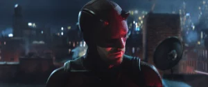 Charlie Cox as Daredevil in red suit on Hell's Kitchen rooftop at night, city lights behind him